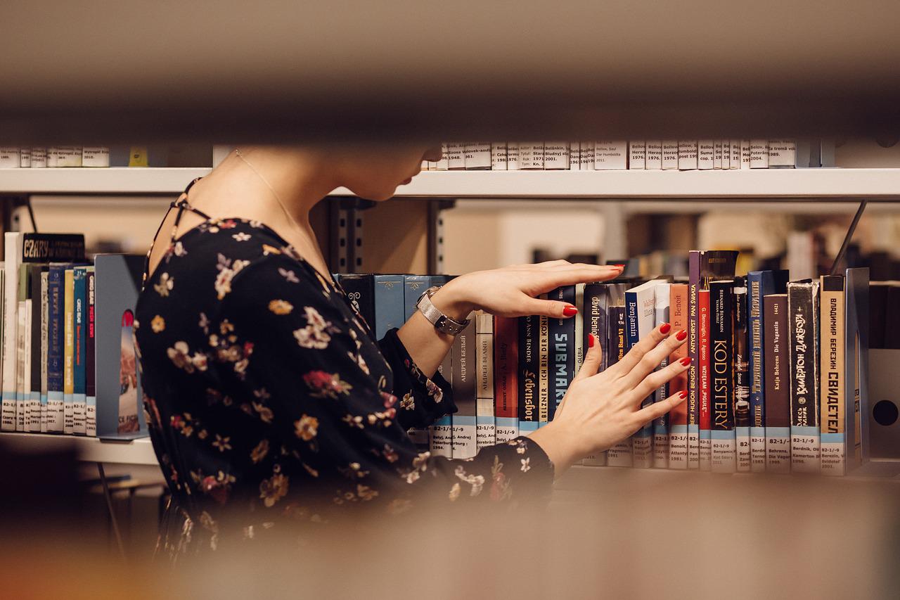 Una lettrice sceglie un libro tra gli scaffali di una biblioteca
